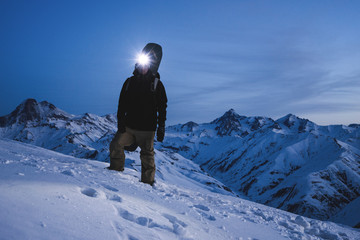 Man with headlamp and backpack wearing ski wear standing in front of amazing winter mountain view. Traveler climb at night on the snowy mountain. Ski tour © leonidkos