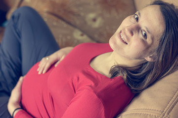 Expecting mother wearing red shirt casualy sitting on a couch.