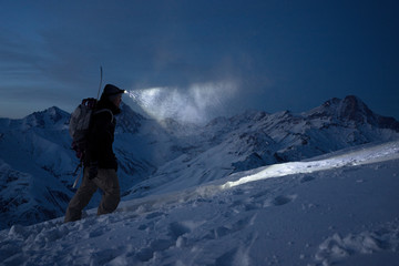 Brave night explorer climbs on high snowy mountains and lights the way with a headlamp. Extreme...