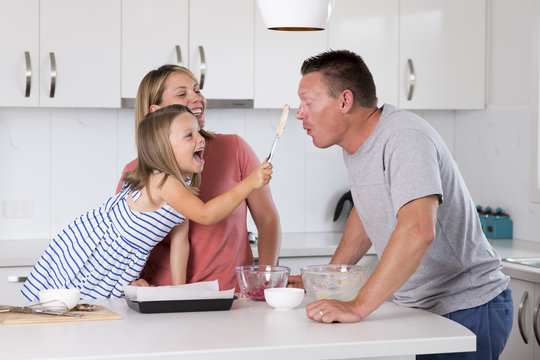 young happy couple baking together with little young beautiful daughter at home kitchen having fun playing with cream in family lifestyle