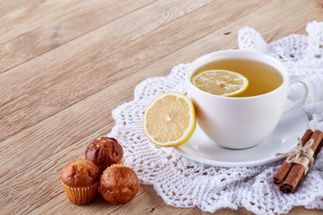 Gourmet tea cup with lemon, cinnamon sticks and tasty muffins on a knitted napkin