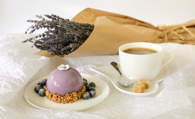 Sweet morning breakfast time concept, beautiful violet cake, blueberries, cup of coffee near bouquet of lavender on white background.