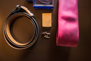 Groom’s accessories: golden cufflinks, cigarette Lighter, black leather belt and a red necktie out of focus