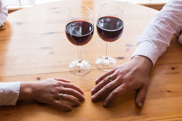 The hand of a man with a ring stretches to the woman's hand. Two glasses with red wine. Romantic dinner, a date. The hand of couple in love with wedding rings