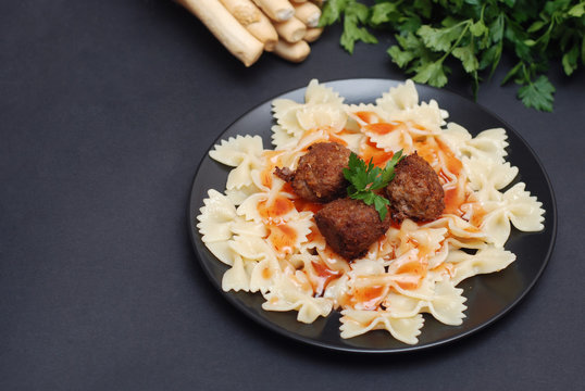 Farfalle Pasta with Meatballs and Sauce on Black Plate. Healthy Food. Dark Background for copy Space for Text.