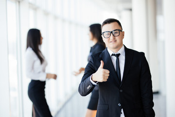Leading my team to success. Handsome young businessman in smart casual wear keeping thumbs up and smiling while his colleagues talking in the background