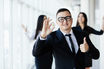 Blockchain and investment concept. Business man leader with thumbs up holding bitcoin in front of his team with raised hands on office.