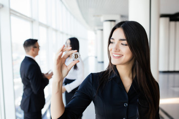 Blockchain and investment concept. Business woman leader holding bitcoin in front of discussing team on office.