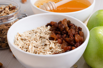 Healthy Breakfast. Oatmeal with raisins in white bowl. Almonds, apple,  honey on white  table background