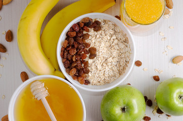Healthy Breakfast. Oatmeal with raisins in white bowl. Two green apples, bananas, honey, nuts