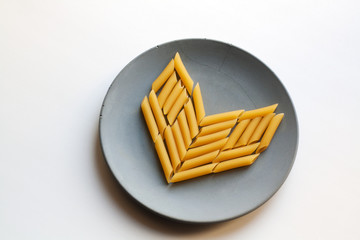 Penne rigate pasta heart isolated on grey concrete plate