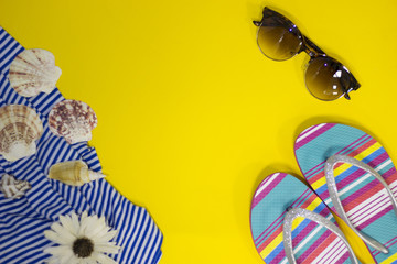 A bright yellow background with beach cloth, slippers and sunglasses, top view. Travel and tourism concept. Space for a text or product display.