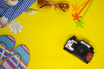 Travel or tourism concept. A bright yellow background with tourist items-camera, beach cloth and slippers, top view. Space for a text or product display.