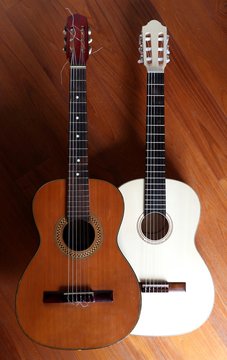 Two acoustic guitars, one light and one dark, side by side on a wooden background