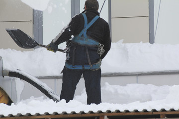 Worker removing snow from a roof with a snow shovel