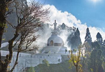 Japanese shanti-stupa, aka Peace pagoda, on the top of mountain in the Darjeeling, in a haze of the arising clouds which penetrate sunshine.