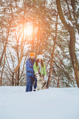 Fototapeta na wymiar Young couple having fun with a dog in forest on vacations. Sun glare effect. Alaskan malamute with family in winter park outdoor.