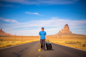 Young traveler with a suitcase walking on a road in Arizona