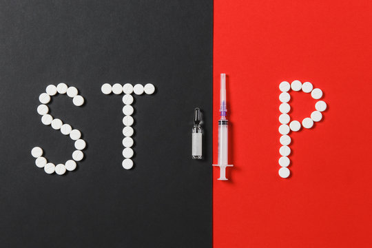 Medication white round tablets in word Stop. Stop medicine violation or against unethical medical business, ampoule, empty syringe needle on red black background. Copy space advertisement.