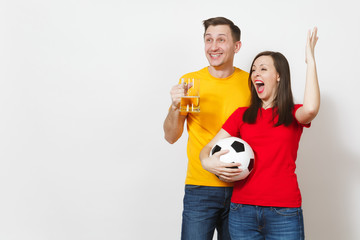 Fun crazy young couple, woman, man, football fans in yellow red uniform cheer up support team with pint mug of beer, soccer ball isolated on white background. Sport, family leisure, lifestyle concept.