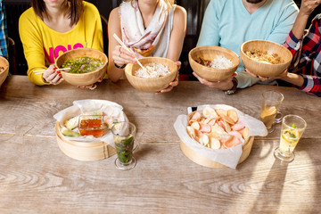 Friends eating asian food sitting at the wooden table