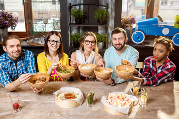 Young friends having fun during the dinner with asian food sitting at the modern restaurant