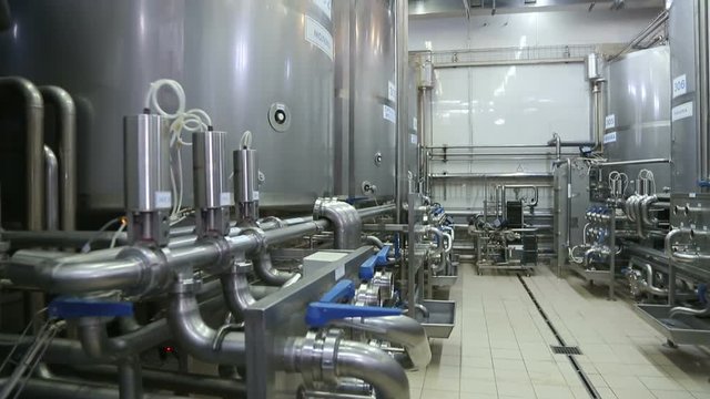 Pipeline in modern dairy factory. Modern complex technological industrial equipment. Plurality of pipelines, gauges and faucets. Shot in motion. Huge tanks for fermenting milk at dairy factory.