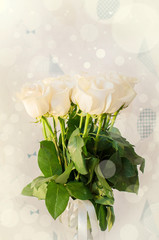 White roses in a high glass vase. Bokeh lights background.