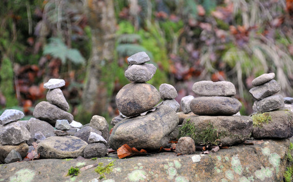 stacked towers of stones and pebbles in woodland on a large rock