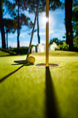 Mini Golf yellow ball with a bat near the hole at sunset