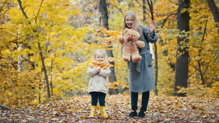 Fototapeta premium Śliczna mała córka z mamą bawi się żółtymi liśćmi w jesiennym parku
