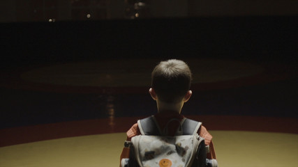 Boy with a backpack in the gym. Boy goes on training on judo in the dark coming to light