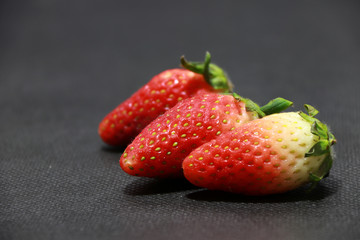 Three Strawberry on the black floor. it is a sweet soft red fruit with a seed studded surface.