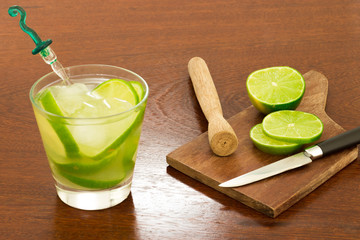 A glass of Caipirinha, is the most famous brazilian drink - lemon cachaca and ice - wood board - slice of lemon - knife on a wood table - 45 angle