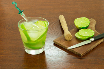 A glass of Caipirinha, is the most famous brazilian drink - lemon cachaca and ice - wood board - slice of lemon - knife on a wood table - 45 angle