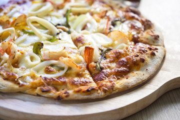 delicious hot crispy pizza with seafood (shrimp, squid, crab, cheese and so on) on a wooden board