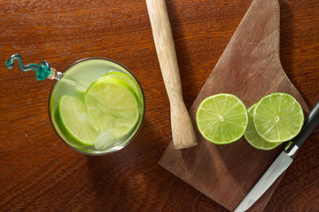 A glass of Caipirinha, is the most famous brazilian drink - lemon cachaca and ice - wood board - slice of lemon - knife on a wood table - top view 