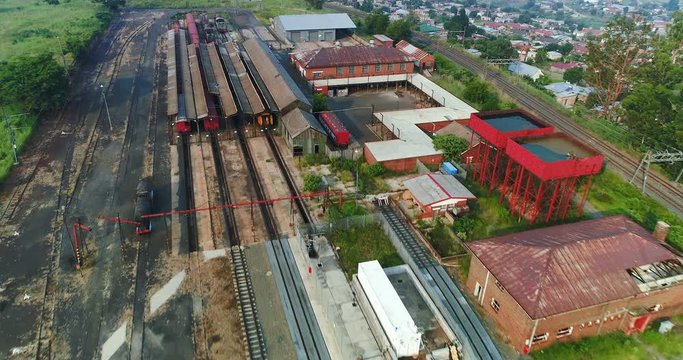 Overhead flight over rusty train yard with semi urban settlements in the distance 4K aerial