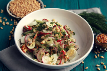 Salad with vegetables and eggs on the colorful blue background. Close up. European cuisine. Radish, cucumber, quail eggs and pine nuts. Ovo vegetarian dish.