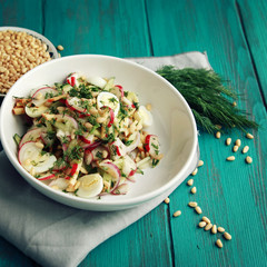 Salad with vegetables and eggs on the colorful blue background. Close up. European cuisine. Radish, cucumber, quail eggs and pine nuts. Ovo vegetarian dish. Toned photo.