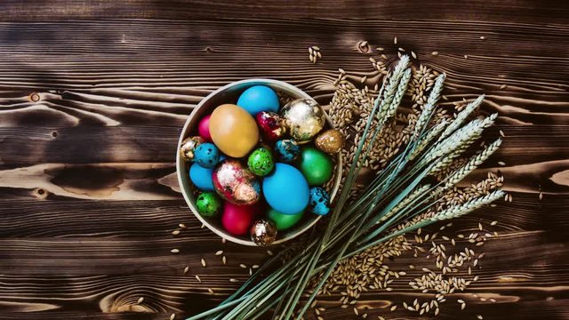 Easter beautiful eggs lie in wooden bowl on wooden table. Around grain, bunch of live ears wheat. Colorful pastel easter eggs on wooden board background with space vintage toned.
