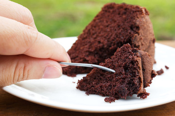 Closeup woman hand use fork to slice chocolate cake.