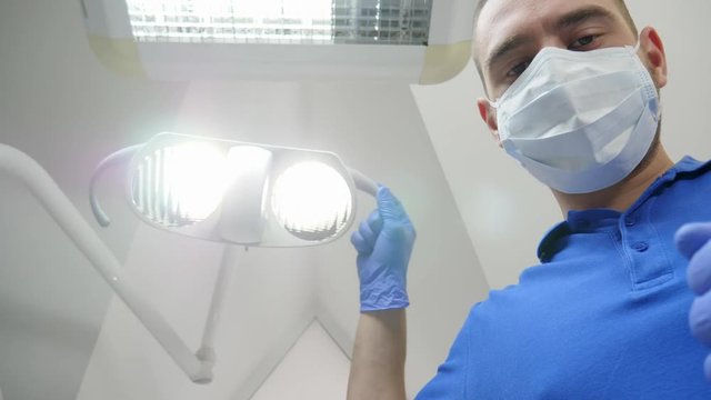 male doctor in medical mask adjusts lighting on background ceiling, patient point of view