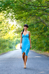 Pretty young brunette woman walking on the empty road at summer day