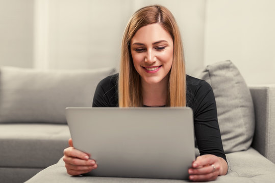Attractive woman using a laptop while lying on the couch at home.