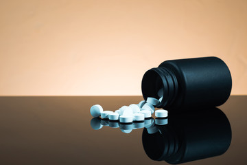 Black Bottle for pills on a black glass table. Beautiful yellow  background.