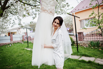 A portrait of a pretty bride posing next to her dress outdoors next to the blossoming tree.