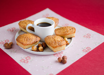 Cakes with caramelized sugar and almond on white plate with cup of coffee on red background