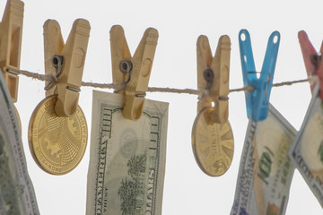 Money laundering concept. Yellow clothes peg hold Bitcoin and one hundred dollar banknotes
