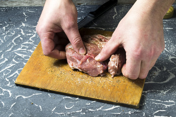 Men's hands rub spices into raw meat.